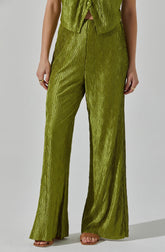 A person is wearing a matching set of shiny, textured olive green clothing. The top is sleeveless with buttons down the front and a small opening at the waist. The pants are high-waisted, wide-legged, and have a crinkled, shiny fabric that creates a textured appearance. The person is also wearing open-toed sandals and several rings on their fingers.